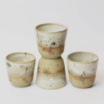 ceramiczne kubeczki z beżowej gliny szkliwione szaro-piaskowym szkliwem pochlapane na grafitowo z niebiesko-zielonymi przebarwieniami