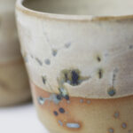 ceramiczne kubeczki z beżowej gliny szkliwione szaro-piaskowym szkliwem pochlapane na grafitowo z niebiesko-zielonymi przebarwieniami