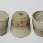 ceramiczne kubeczki z beżowej gliny szkliwione szaro-piaskowym szkliwem pochlapane na grafitowo z niebiesko-zielonymi przebarwieniami